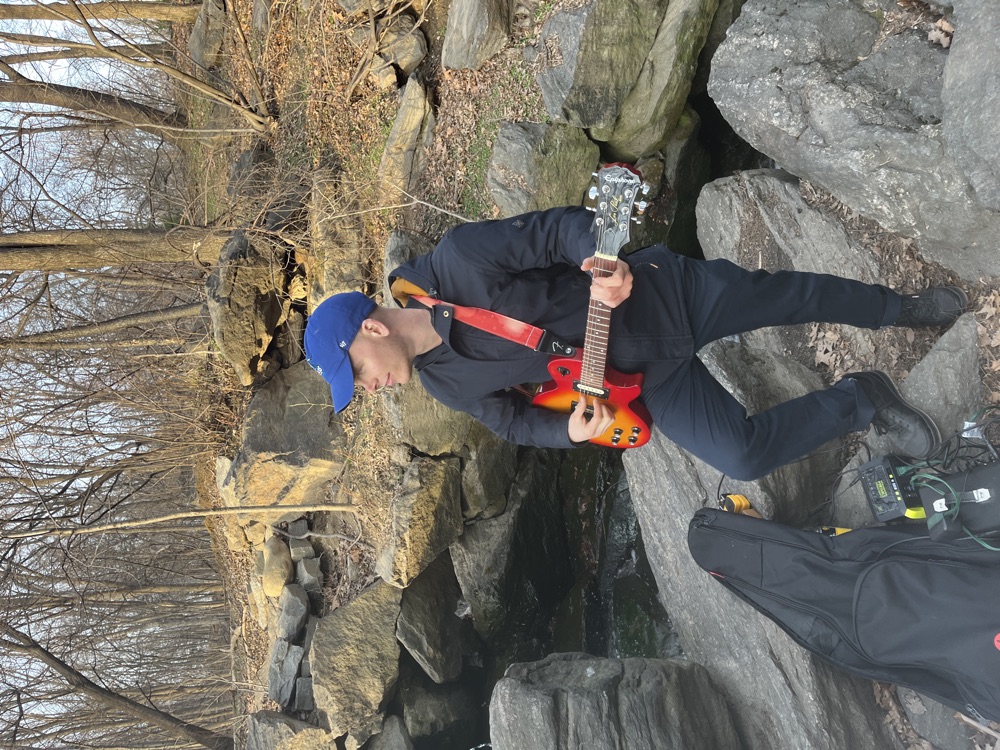 Olivier playing electric guitar beside a rocky stream